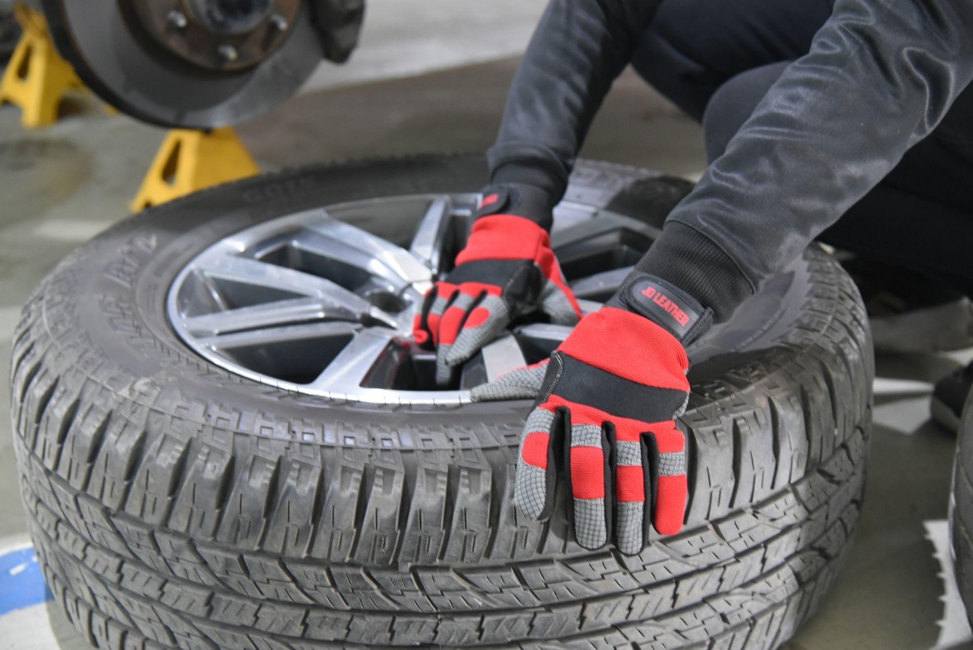 A person wearing red gloves works on a car tire.